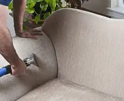 Professional upholstery cleaner deep-cleaning a fabric sofa with a handheld extraction tool and hose in Springfield, MO.